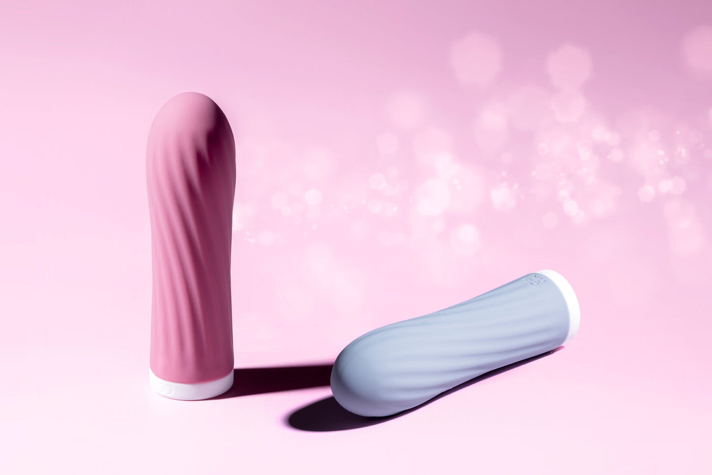 Pink bullet vibrator standing upright, blue bullet laying down, pink background
