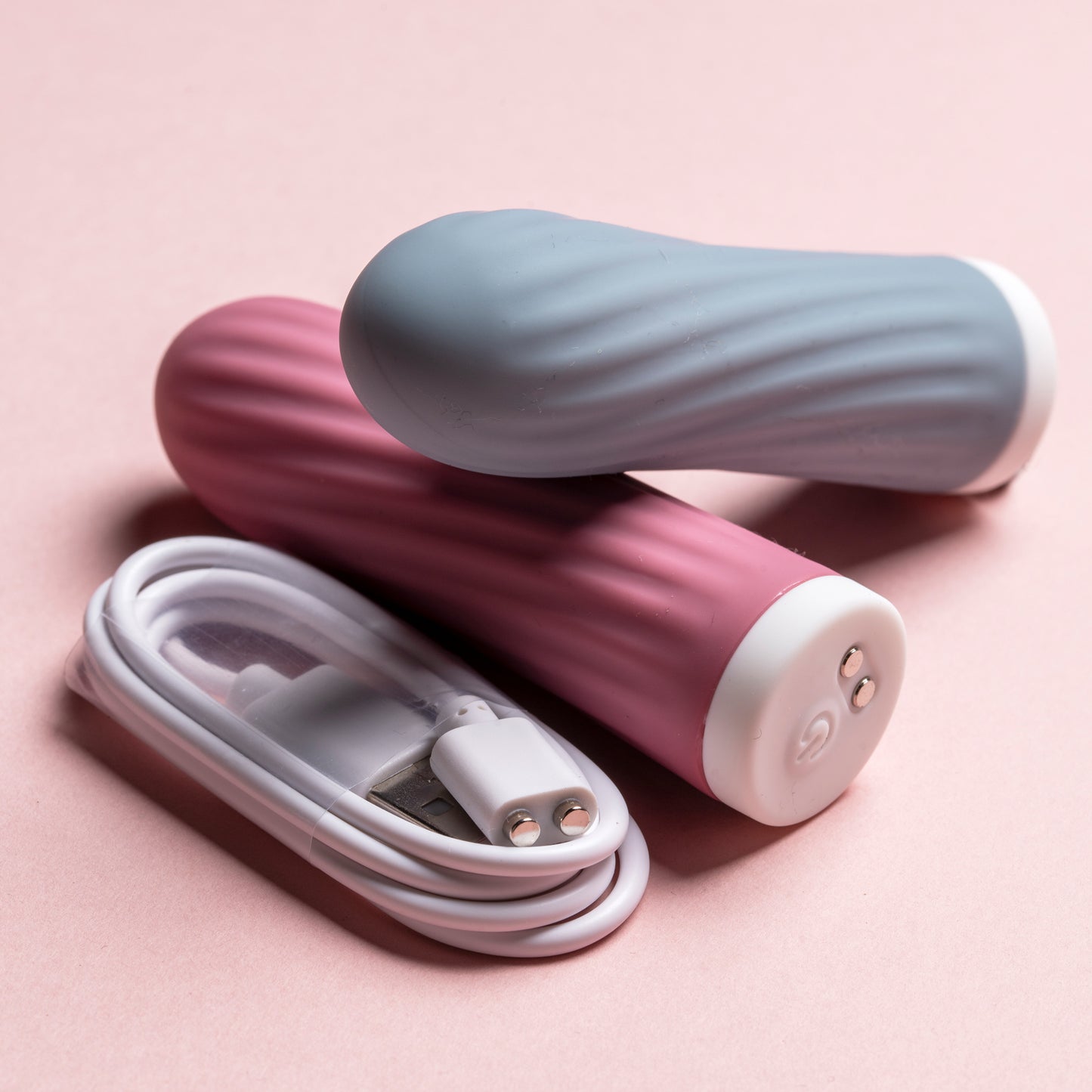 Pink bullet laying down with blue bullet resting on it, charging cable beside them