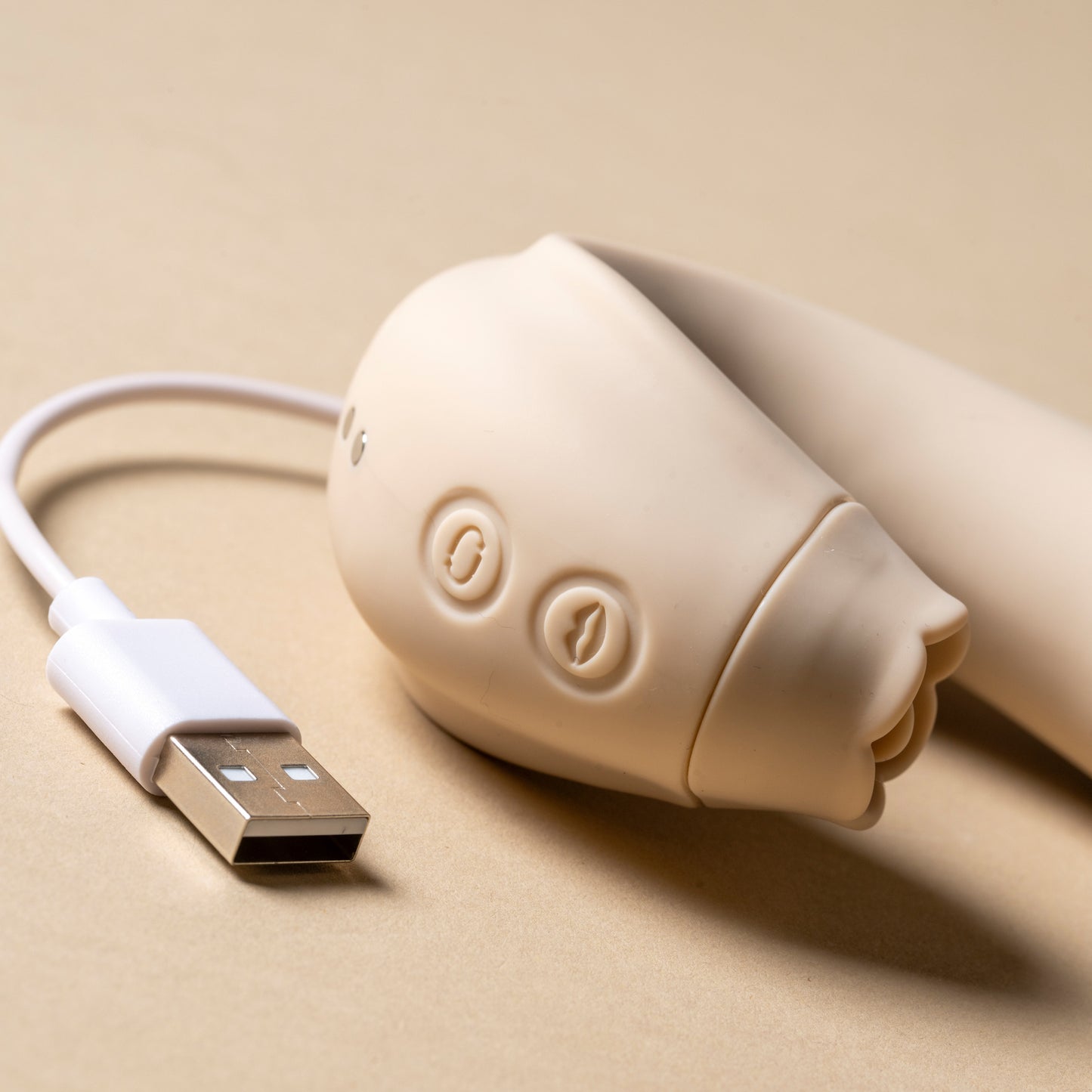 Close-up of licking feature with charging lead beside vibrator, cream background