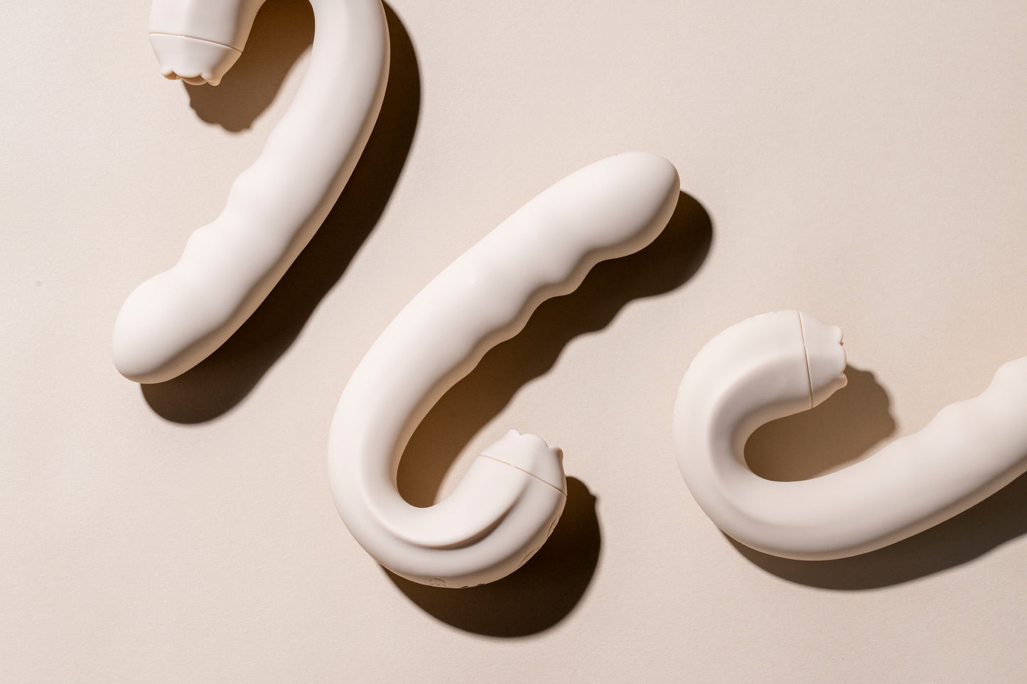 Three vanilla clitoral licking vibrators laying down on cream background