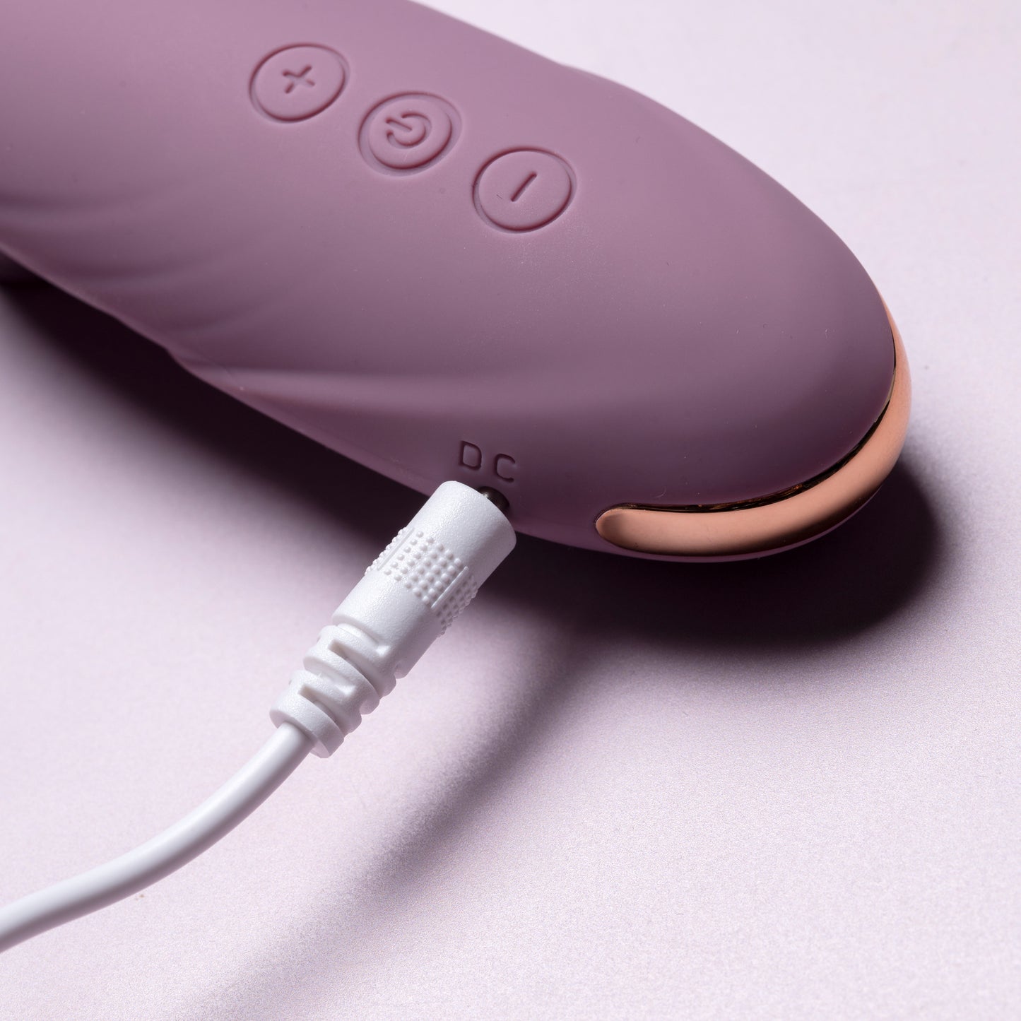 Pink clitoral suction vibrator with charging cable inserted, close-up on pink surface