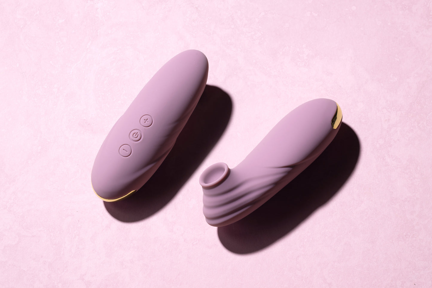 Two pink clitoral suction vibrators laying side by side, pink background