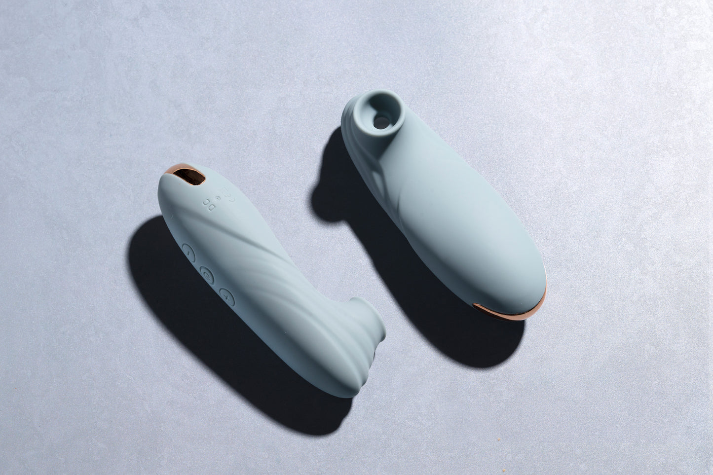Two teal clitoral suction vibrators laying on blue surface