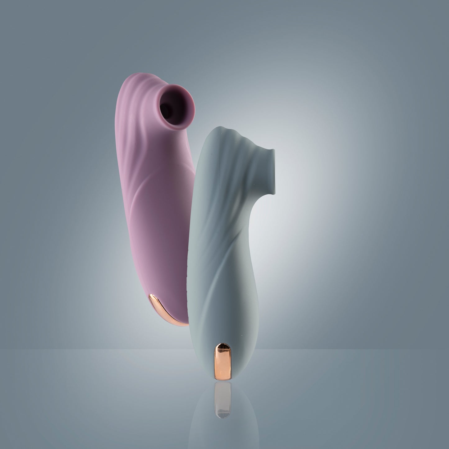 Teal clitoral suction vibrator standing on reflective blue surface with pink one suspended in the air