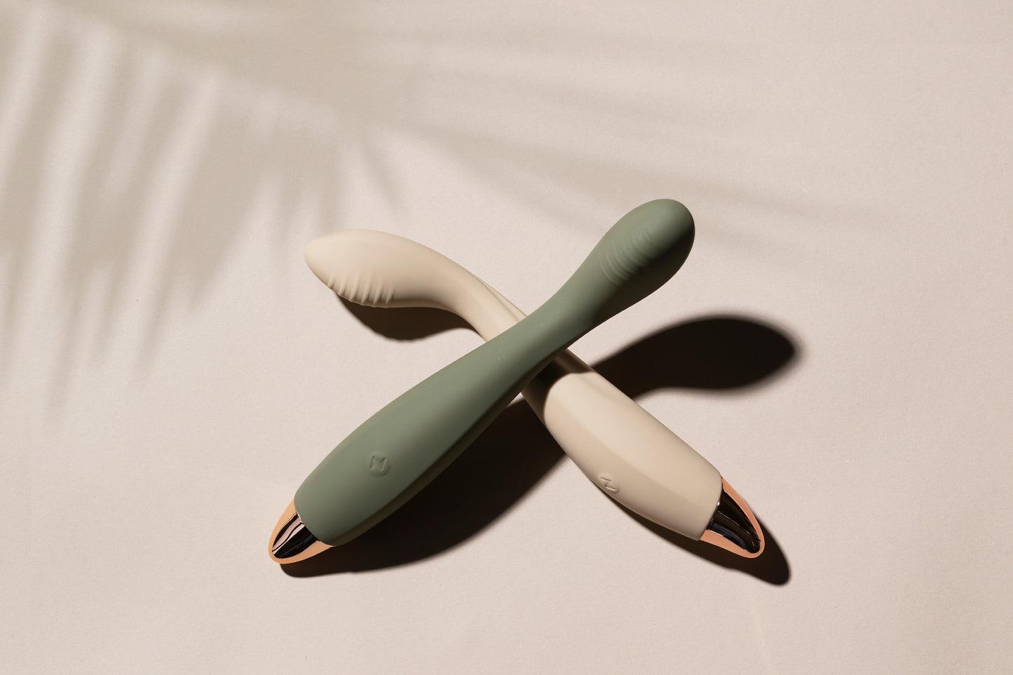 Vanilla G-spot vibrator laying down with green vibrator resting on it, palm leaf shadow in background