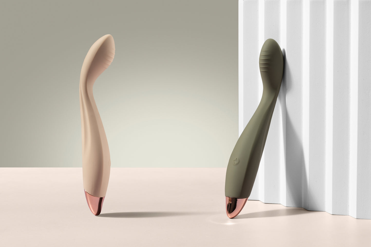 Vanilla and green G-spot vibrators standing upright, green one leaning on white prop