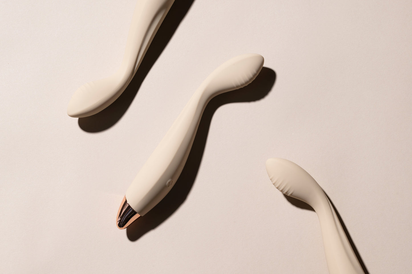 Three vanilla G-spot vibrators laying down on cream surface