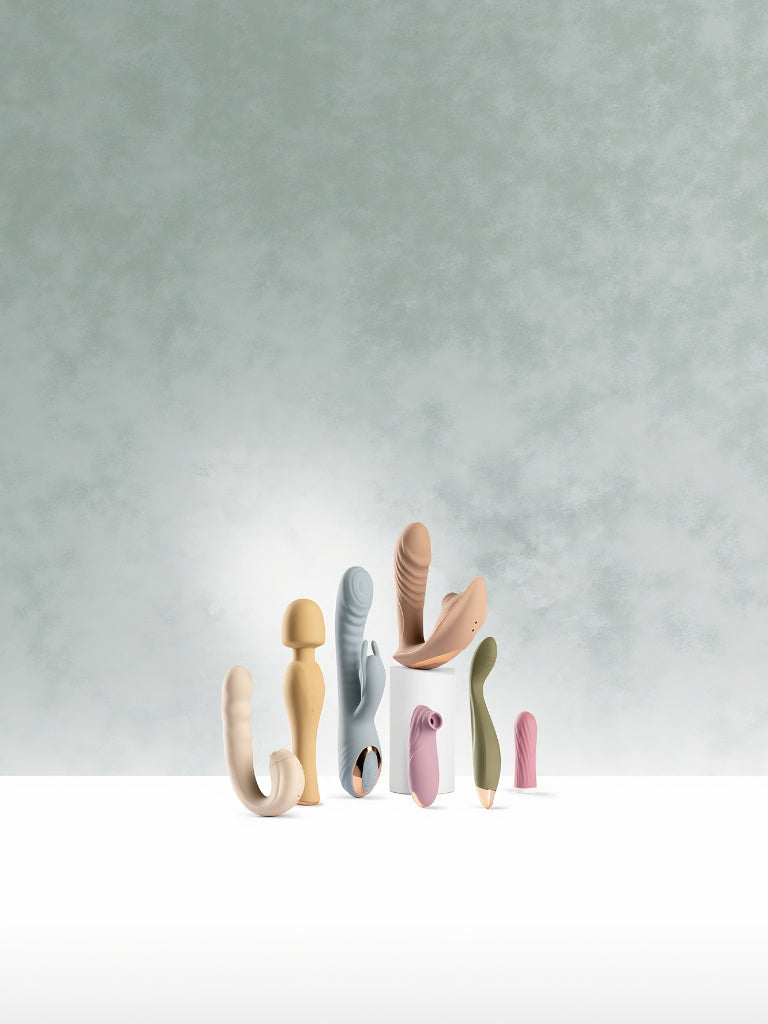 Elegant lineup of SmootherVibes body-safe vibrators including rabbit, wand, G-spot, and clitoral designs on white pedestal background.